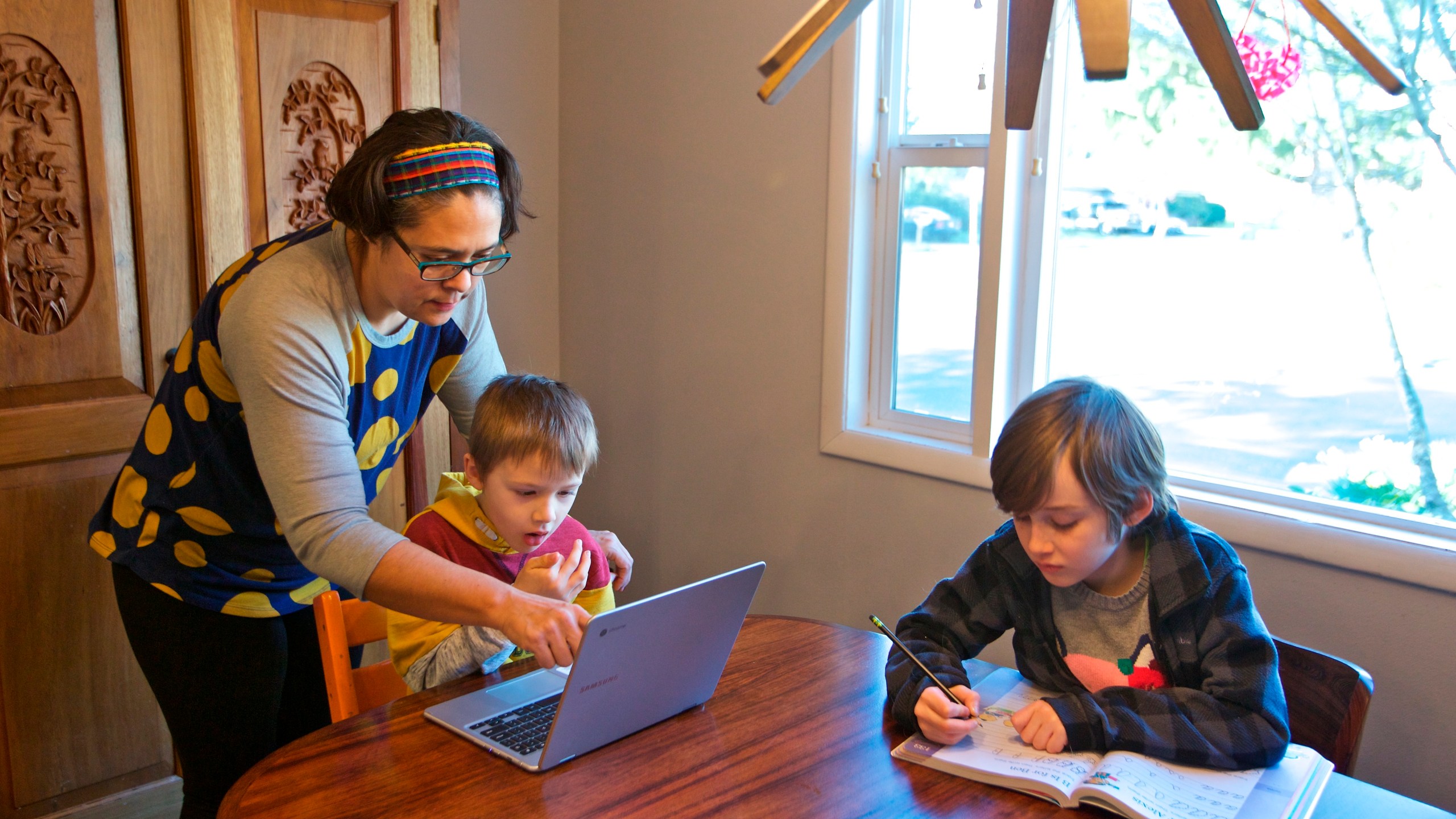 Olivia Bucks, left, helps her son Keith Bucks, center, with an online class assignment while Ashton Morris, right, works on a handwriting lesson from their first grade class at Arco Iris Spanish Immersion School in Beaverton, Ore. Bucks works from home selling books online and now spends her time between working on her business and helping her sons with their school work. They are using her work laptop to access their classroom assignments. (AP Photo/Craig Mitchelldyer)