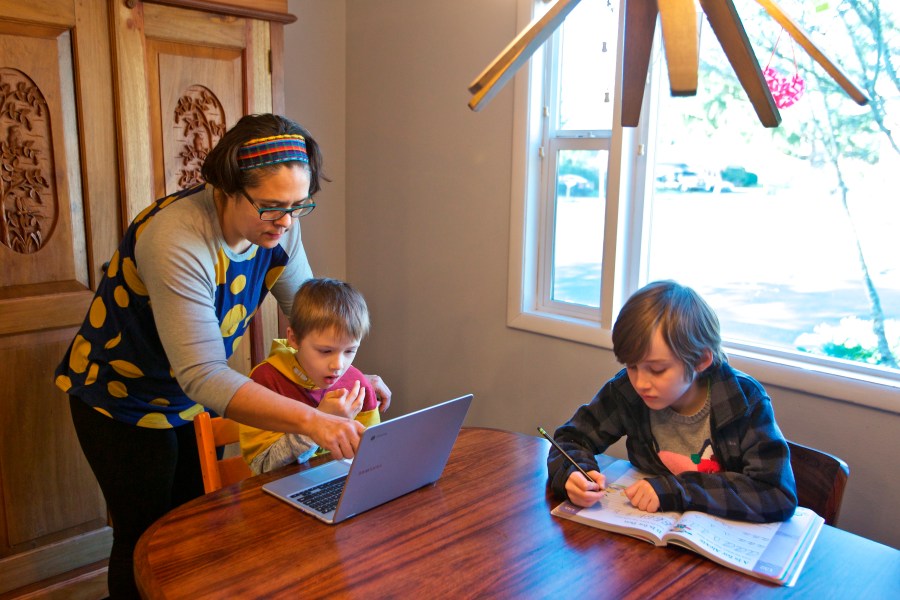 Olivia Bucks, left, helps her son Keith Bucks, center, with an online class assignment while Ashton Morris, right, works on a handwriting lesson from their first grade class at Arco Iris Spanish Immersion School in Beaverton, Ore. Bucks works from home selling books online and now spends her time between working on her business and helping her sons with their school work. They are using her work laptop to access their classroom assignments. (AP Photo/Craig Mitchelldyer)