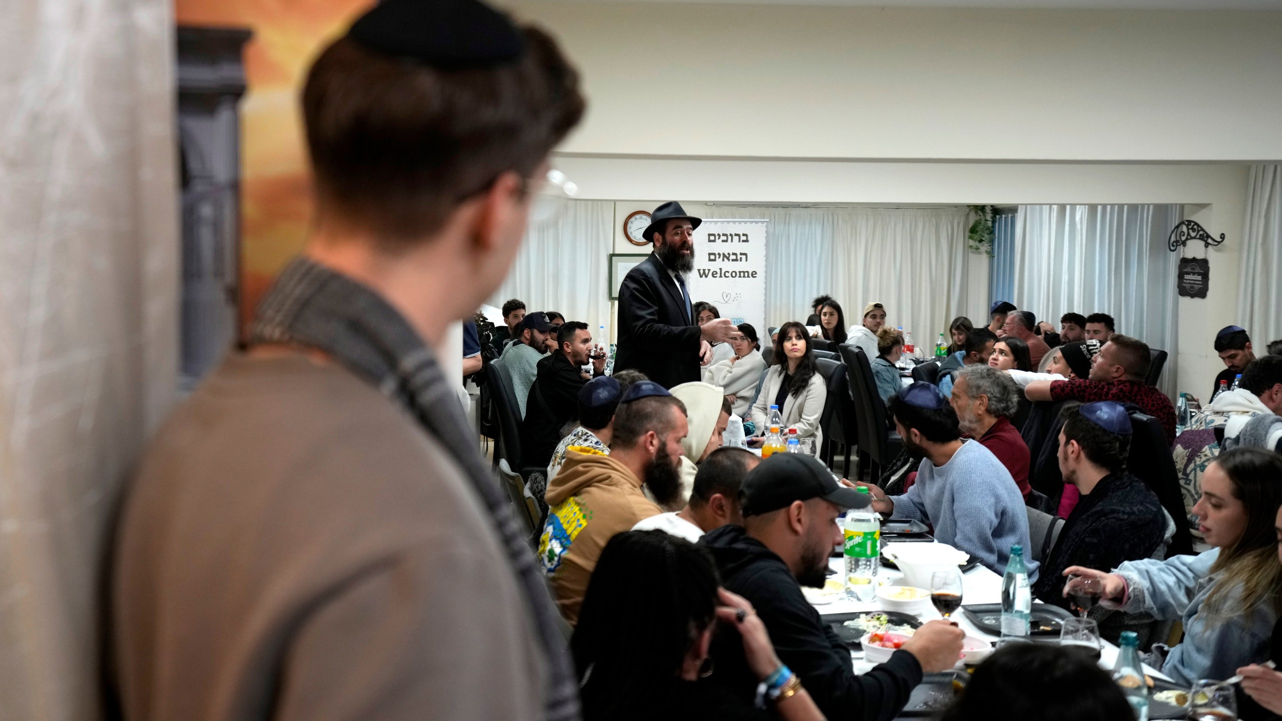 Cyprus' Chief Rabbi Arie Zeev Raskin, background, addresses young people who attended a retreat in Cyprus to help them cope with the psychological trauma they suffered from the Oct. 7 attack by Hamas militants on a rave party in southern Israel, at Cyprus' Jewish Community Center in the southern coastal town of Larnaca, Cyprus, on Thursday, Nov. 30, 2023. (AP Photo/Petros Karadjias)