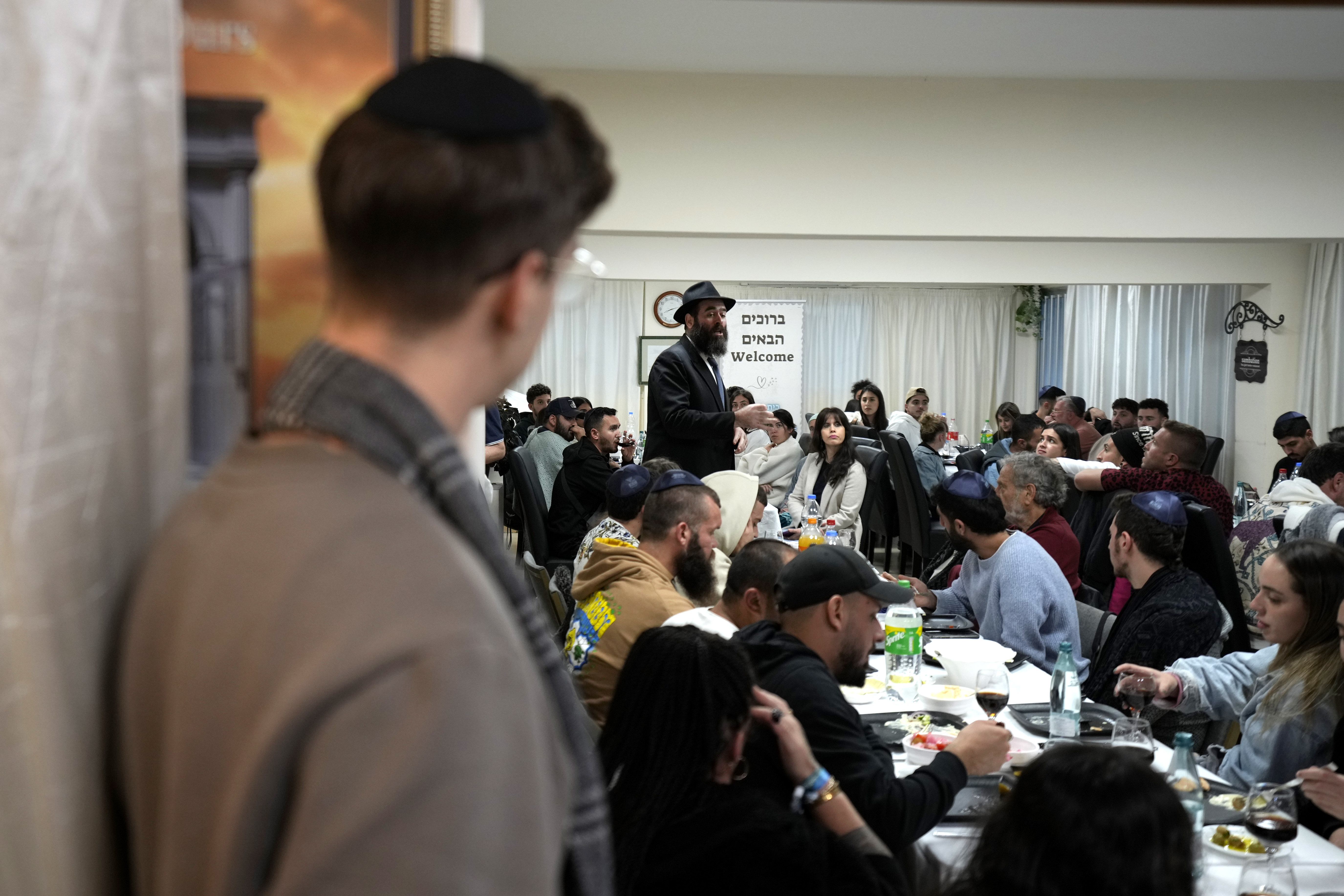 Cyprus' Chief Rabbi Arie Zeev Raskin, background, addresses young people who attended a retreat in Cyprus to help them cope with the psychological trauma they suffered from the Oct. 7 attack by Hamas militants on a rave party in southern Israel, at Cyprus' Jewish Community Center in the southern coastal town of Larnaca, Cyprus, on Thursday, Nov. 30, 2023. (AP Photo/Petros Karadjias)