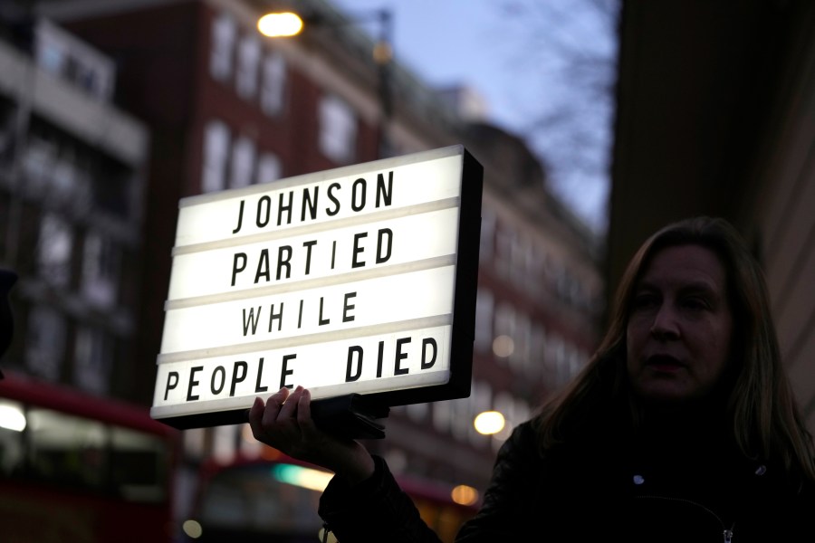 A demonstrator holds a banner after Britain's former Prime Minister Boris Johnson arrived to give evidence at the Covid-19 Inquiry in London, Wednesday, Dec. 6, 2023. (AP Photo/Kirsty Wigglesworth)